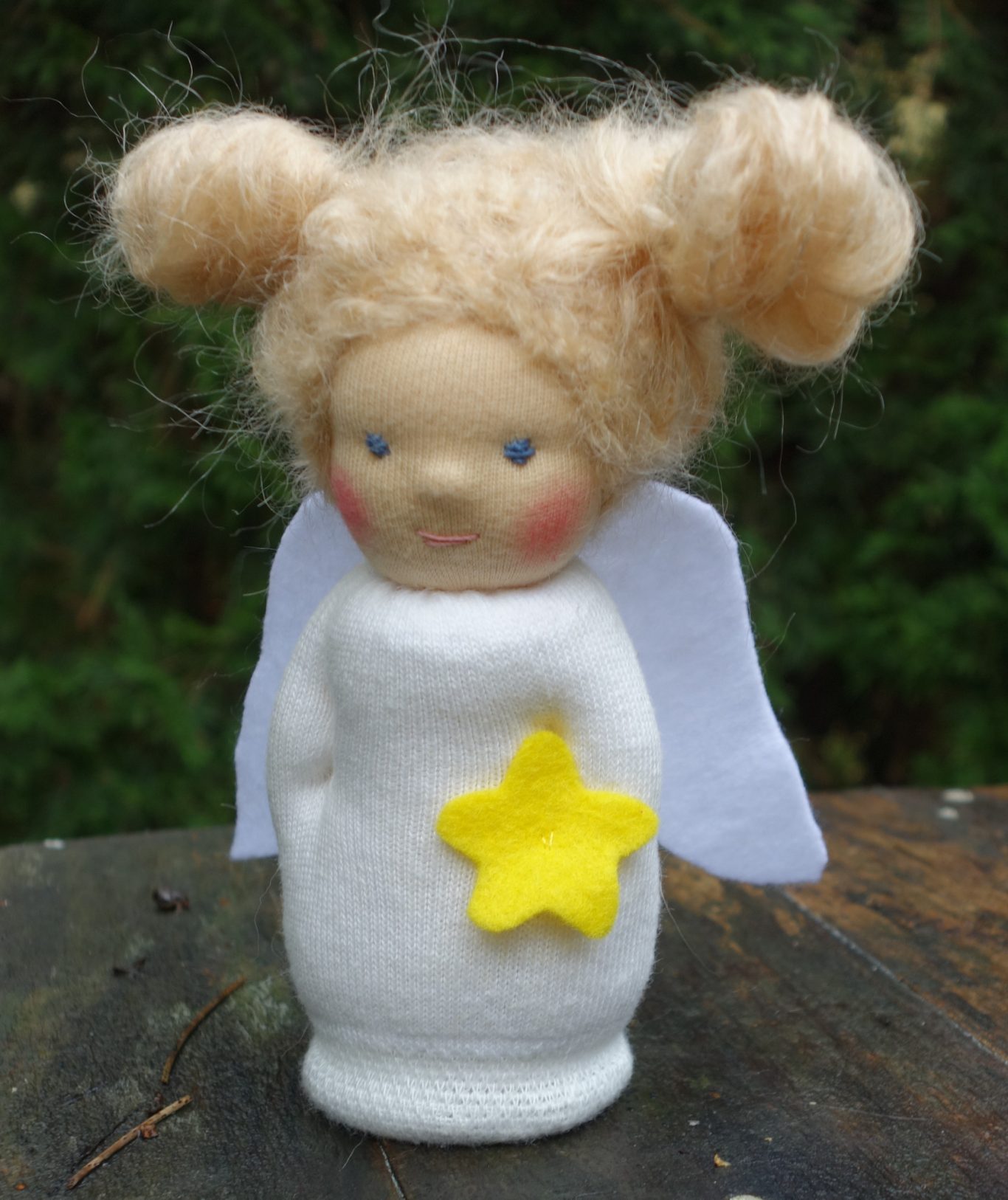 Engelpüppchen mit blonden Haaren und einem leuchtenden gelben Stern aus Filz. Es ist aus einem Sockenschaft genäht und schaut fröhlich.