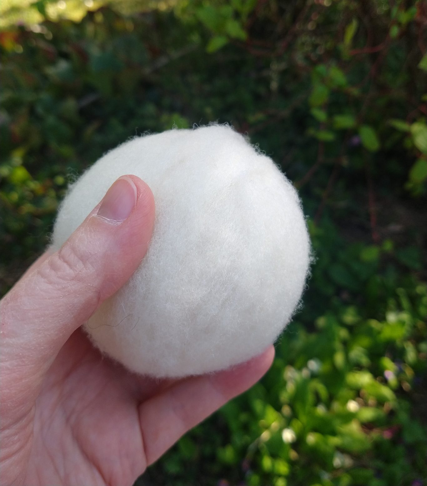 Man sieht meine Hand, die einen gefilzten Ball aus Schafwolle hält. Dieser dient als Grundlage für jeden Puppenkopf.