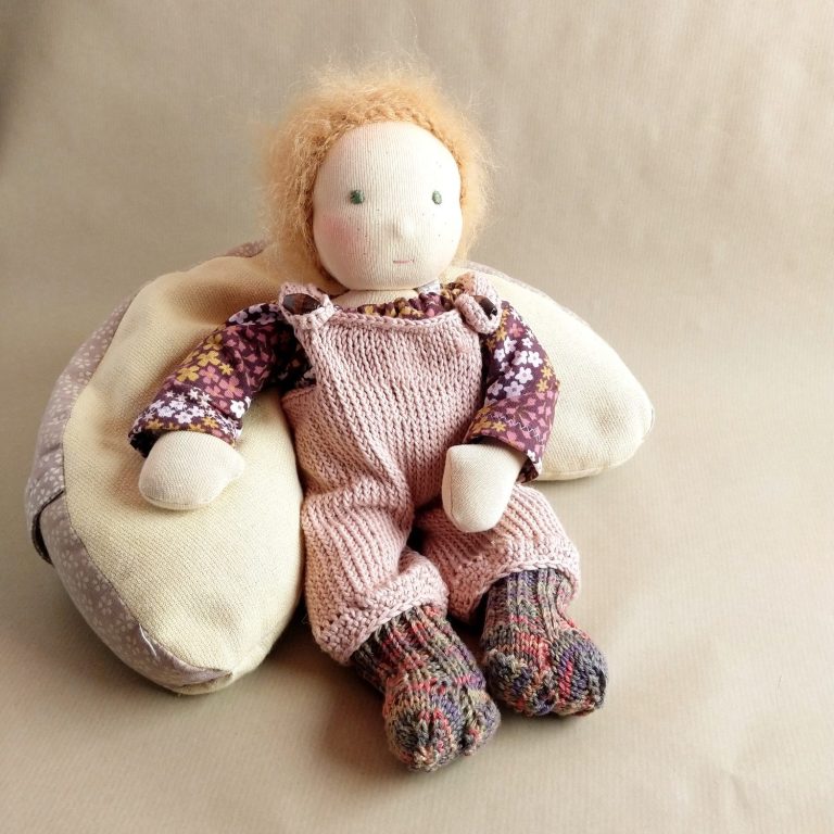 Puppenbaby von Susis Puppenglück Puppenbaby mit roten Wuschelhaaren und grünen Augen. Es trägt eine gestrickte, rosa Latzhose und ein geblümtes Oberteil