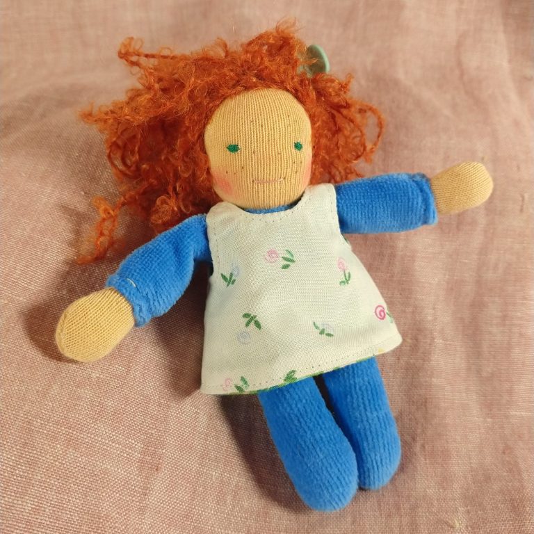 Taschenpuppe von Susis Puppenglück Taschenpuppe mit dunkelblauem Nicky-Körper und weißem Kleid mit Streublümchen. Sie hat rote wilde Locken, grüne Augen und Sommersprossen.