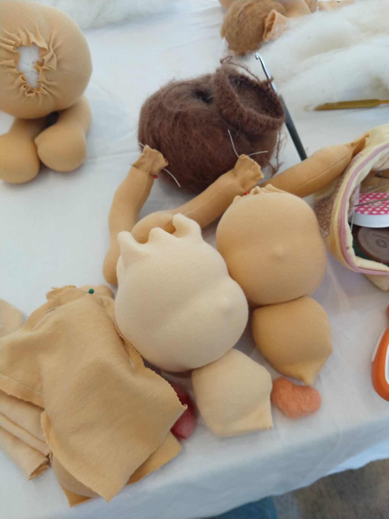 Man sieht 2 Puppenköpfe mit verschiedener Hautfarbe im Fertigungsprozess und ein begonnenes Haarkäppchen. Die Köpfe haben noch kein Gesicht.
