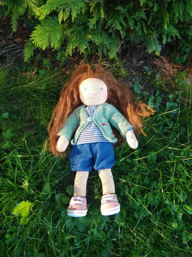 Man sieht eine Gliederpuppe mit langen, braunen Haaren. Sie trägt eine grüne Strickjacke, ein geringeltes Shirt, Jeans und Sneaker.