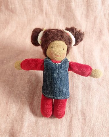 Man sieht eine Taschenpuppe mit rotem Nicky-Körper und braunen Haarschnecken. Sie trägt eine Jeanskleid