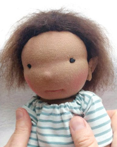 Man sieht Kopf und Oberkörper einer Gliederpuppe mit kurzen, dunkelbraunen Haaren. Sie trägt ein geringeltes Shirt.