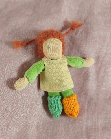 Man sieht eine Taschenpuppe mit grünem Nicky-Körper und roten Zöpfen. Sie trägt ein gelbes Kleid und verschiedenfabige Strümpfe.